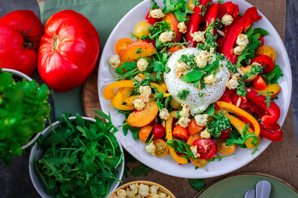 prato com mix de vegetais e mão de pessoa adicionando azeite, vista superior